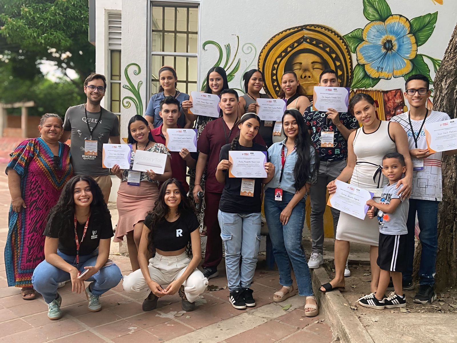 Participants holding Rebel Business School and Mercy Corps certificates in front of a mural